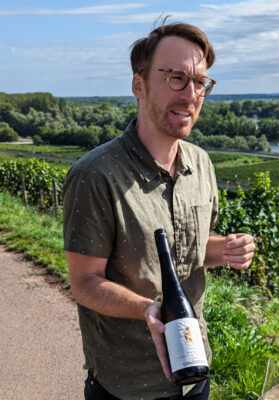 Johannes Hasselbach im Weinberg mit einer Flasche Virgo.